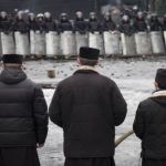 3 كهنة يصلّون في مواجهة صفوف من رجال الشرطة في الموقع الذي شهد أحداث عنف في كييف في 13 شباط 2014. (رويترز)